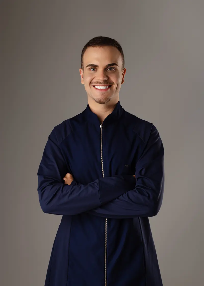 Dr. Kainã Andrade sorrindo, de braços cruzados, com jaleco azul-marinho